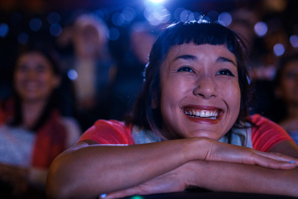 Woman smiling, watching theatre screen. 